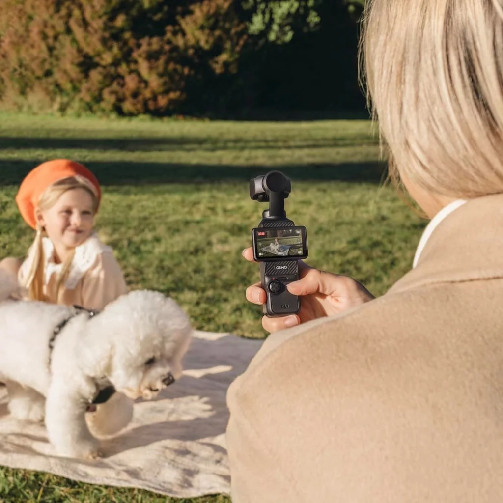 Une femme filme sa fille et son chien au parc avec la DJI Osmo Pocket 3